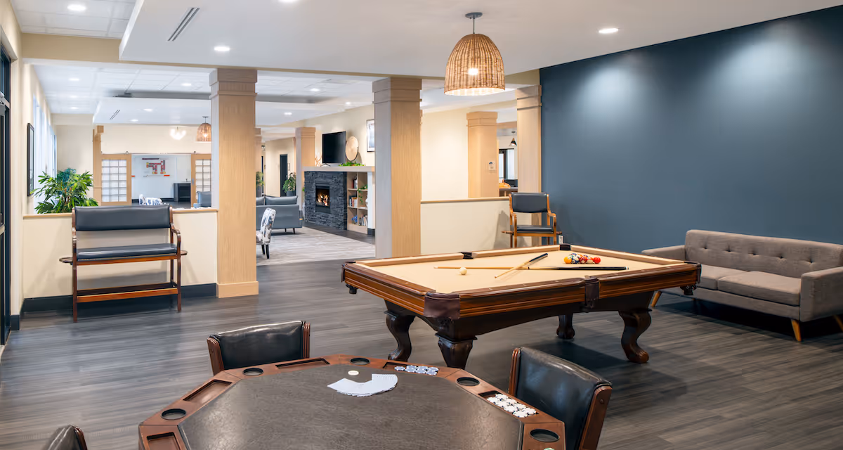 Open recreation room featuring a pool table, card table, sofa and chairs with a fireplace and seating area in the background.
