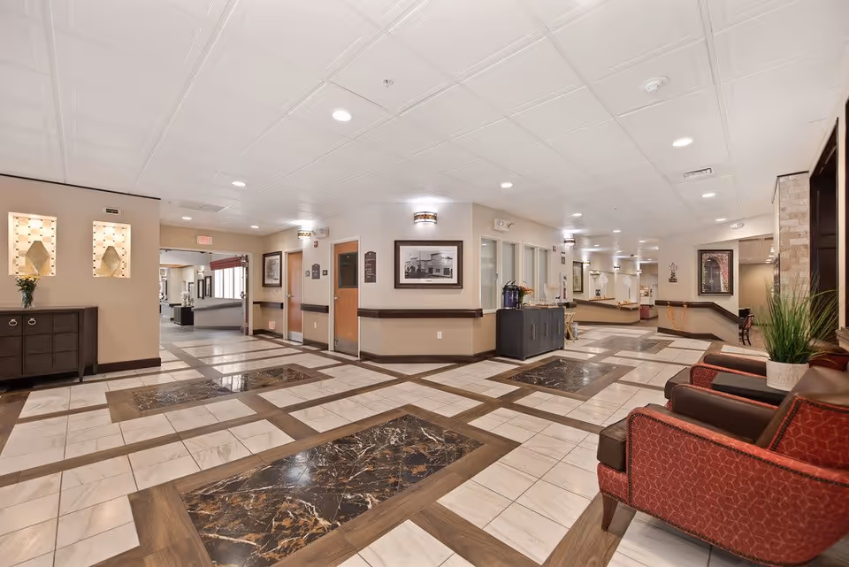 Spacious, well-lit senior living facility lobby with patterned tile floors, seating area, and a reception corridor.