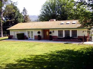 Single-story residence-style senior facility with yellow exterior, front entry, and trimmed lawn.