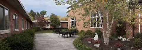 Outdoor courtyard at Coffman Nursing Home with brick buildings, trees, and tables.