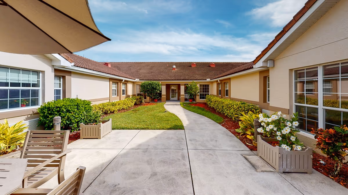 Sunlit landscaped courtyard with a curved concrete walkway, planters and seating between single-story senior living buildings.