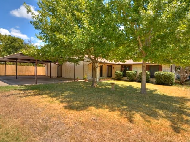 Exterior view of a single-story assisted living facility with trees and a shaded entrance.