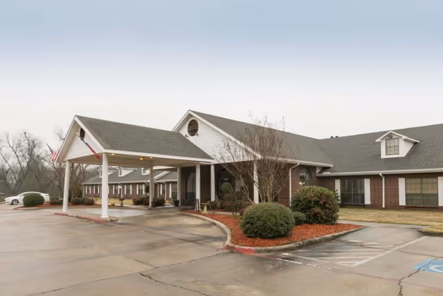 Front entrance of a brick senior healthcare building with a covered porte-cochère and landscaped beds.
