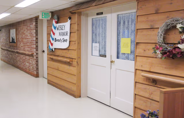 Interior hallway at Wesley Manor showing the Beauty Shop double doors and sign on a wood-paneled wall.