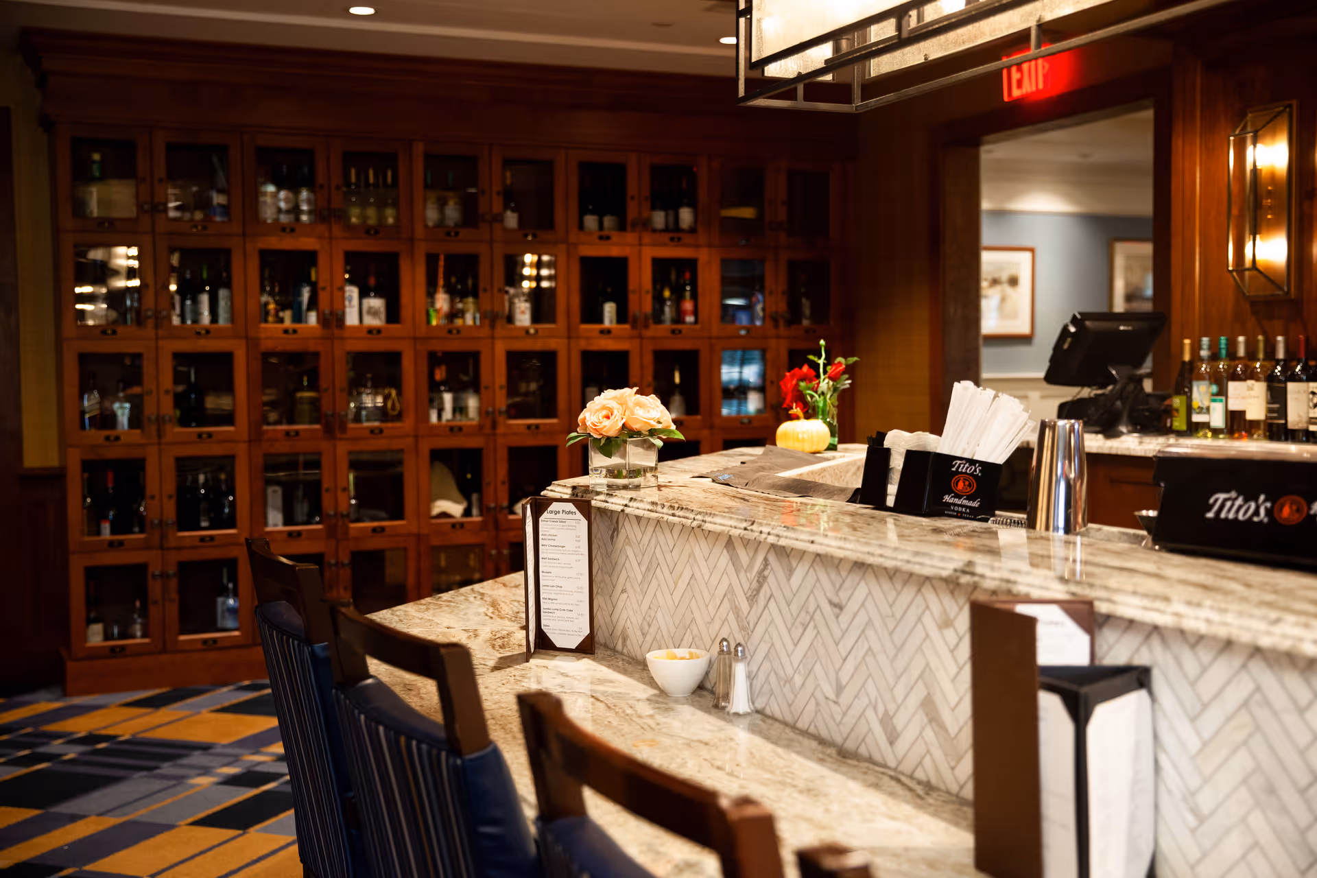 Interior view of a dining/bar area with a marble countertop, bar stools, and wooden wine lockers in the background.