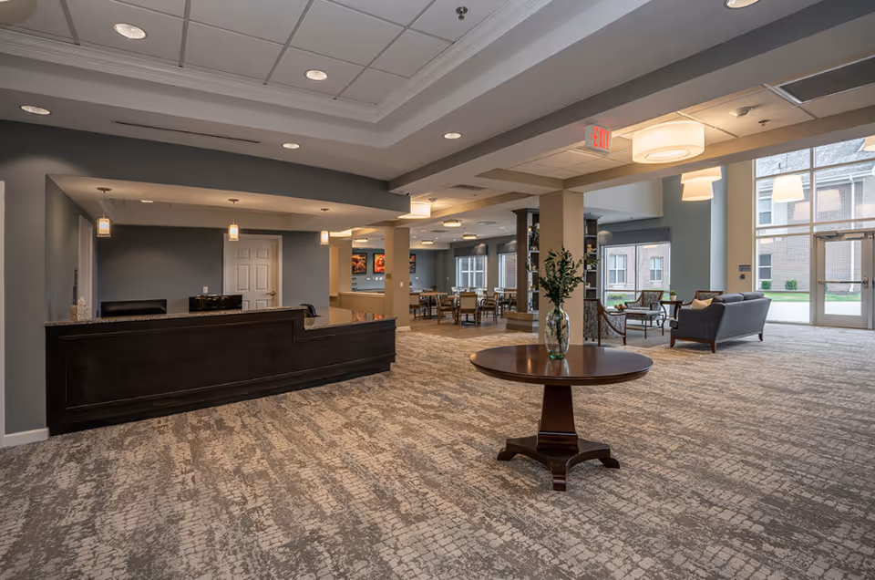 Spacious lobby with dark reception desk, round table, and seating near large windows.