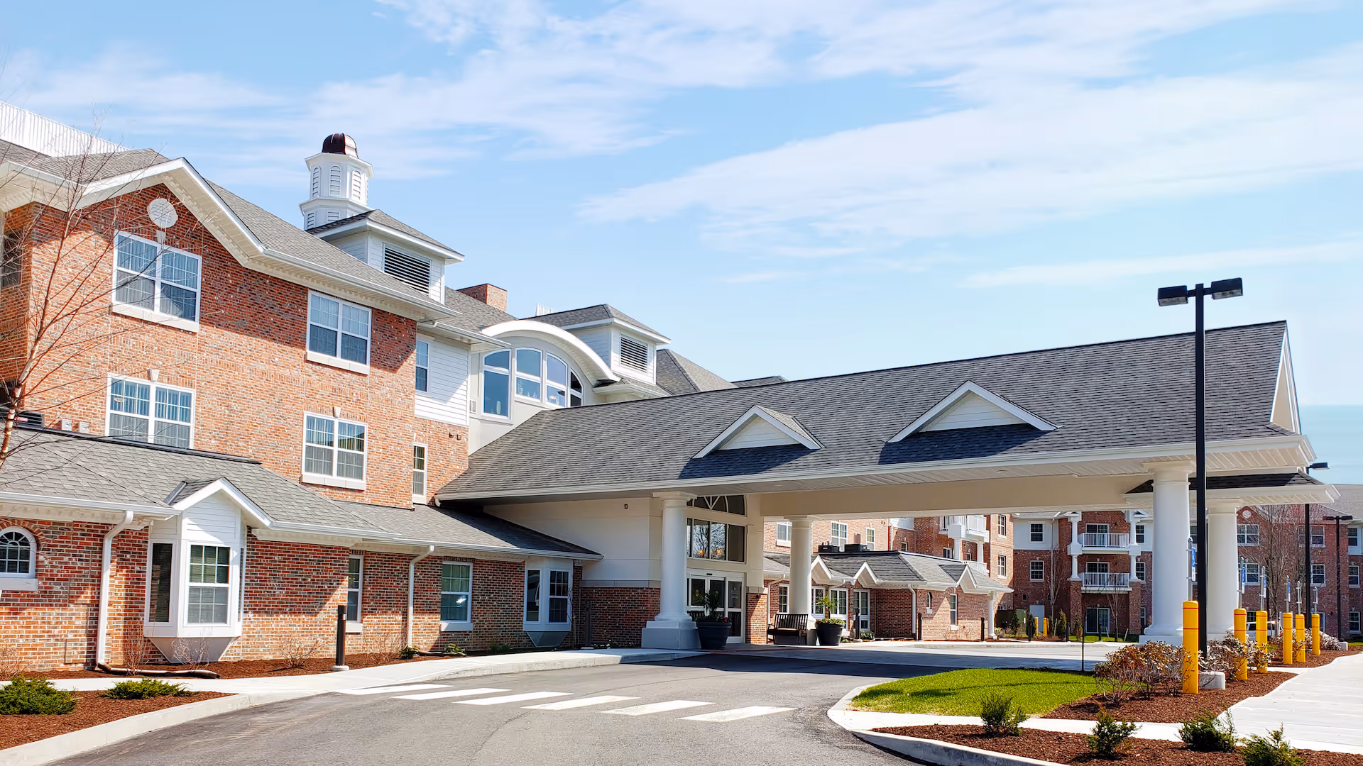 Front exterior of a brick retirement community with a covered porte-cochere entrance and drive.