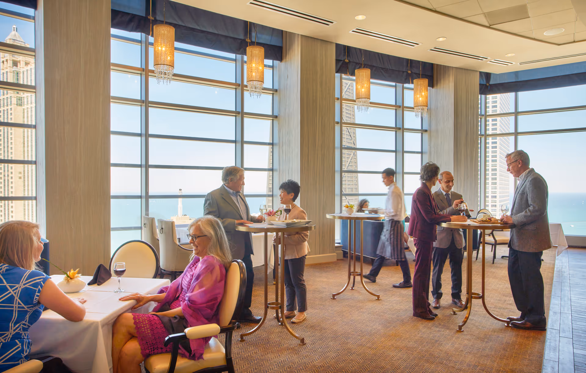Seniors and staff socialize in a bright dining/lounge area with high-top tables and large windows showing city and water views.