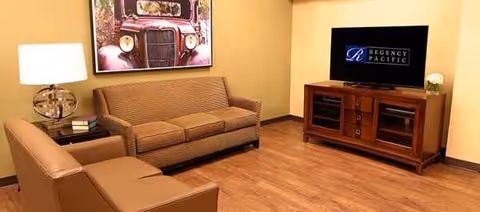 Lobby-style living room with sofa, chairs, TV, and artwork in Regency North Bend Rehab Center.