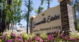 Exterior entrance sign for Summerville Estates Gracious Retirement Living with landscaped flowers.