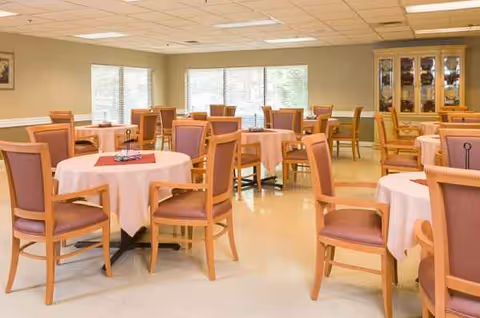 Senior living dining room with round tables, pink tablecloths, and wooden chairs.