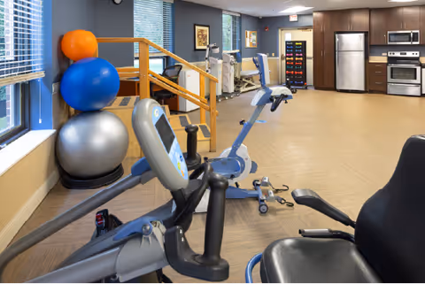Interior fitness/therapy room with exercise bikes, stability balls, hand weights and a kitchenette in the background.