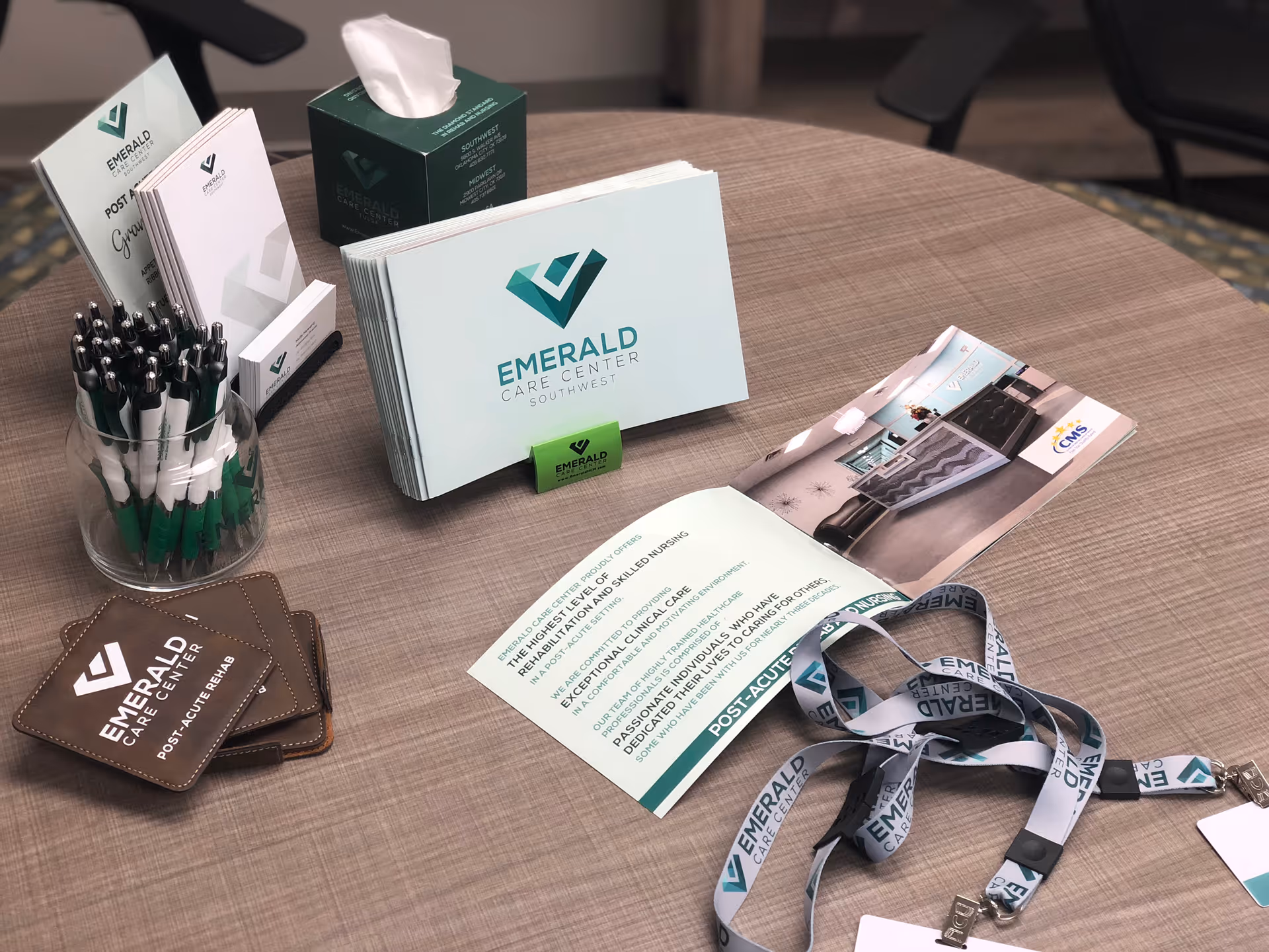 Brochures, pens, lanyards and other promotional materials for Emerald Care Center Southwest arranged on a round table.