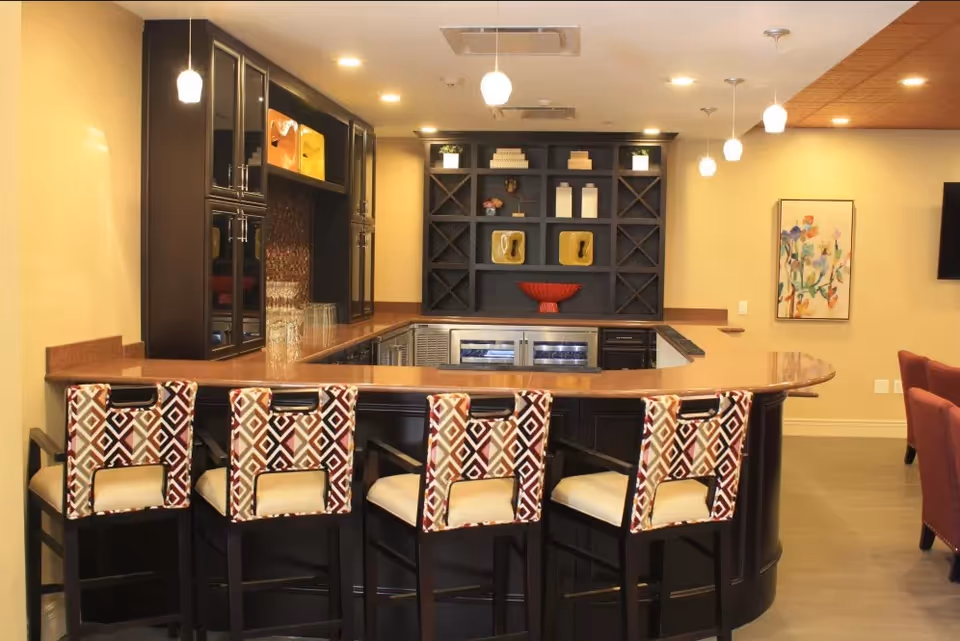 A communal bar area with five patterned barstools around a curved dark wood counter facing built-in shelving and pendant lights.