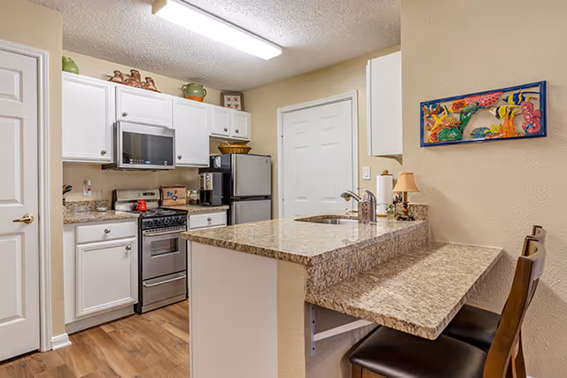 Small modern kitchen with white cabinetry, stainless steel appliances and a granite breakfast bar with two stools.