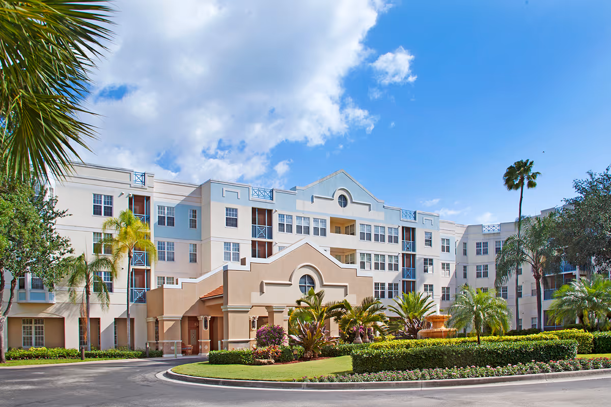Exterior view of a multi-story senior living building with palm trees and a circular driveway.