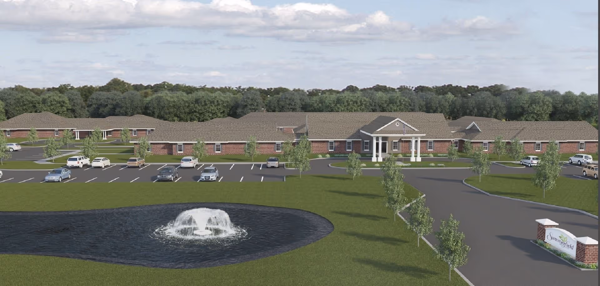 Exterior view of Summerfield Senior Living of Gulfport showing a large single-story brick building with a covered entrance supported by white columns. In front of the building is a circular driveway, a parking lot with several cars, a landscaped lawn with small trees, and a pond with a water fountain. The background features a line of trees under a partly cloudy sky.