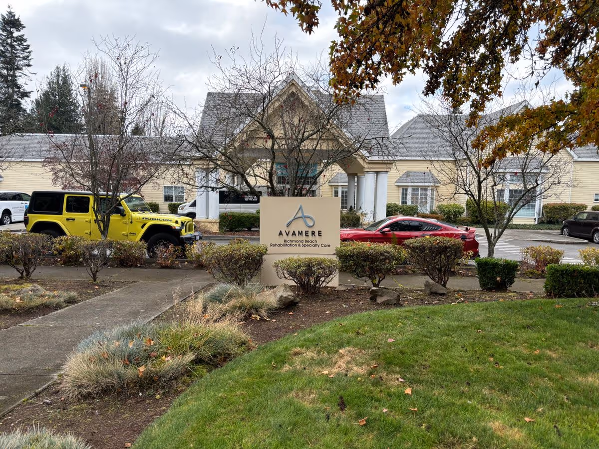Front entrance and sign for Avamere Richmond Beach rehabilitation facility with parked cars and landscaped grounds.