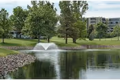 Pond with fountain, trees, and a grassy lawn near Heather Gardens.