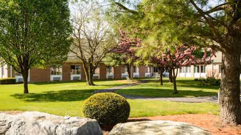 Front view of Carlisle Skilled Nursing and Rehabilitation Center with green lawn and trees.