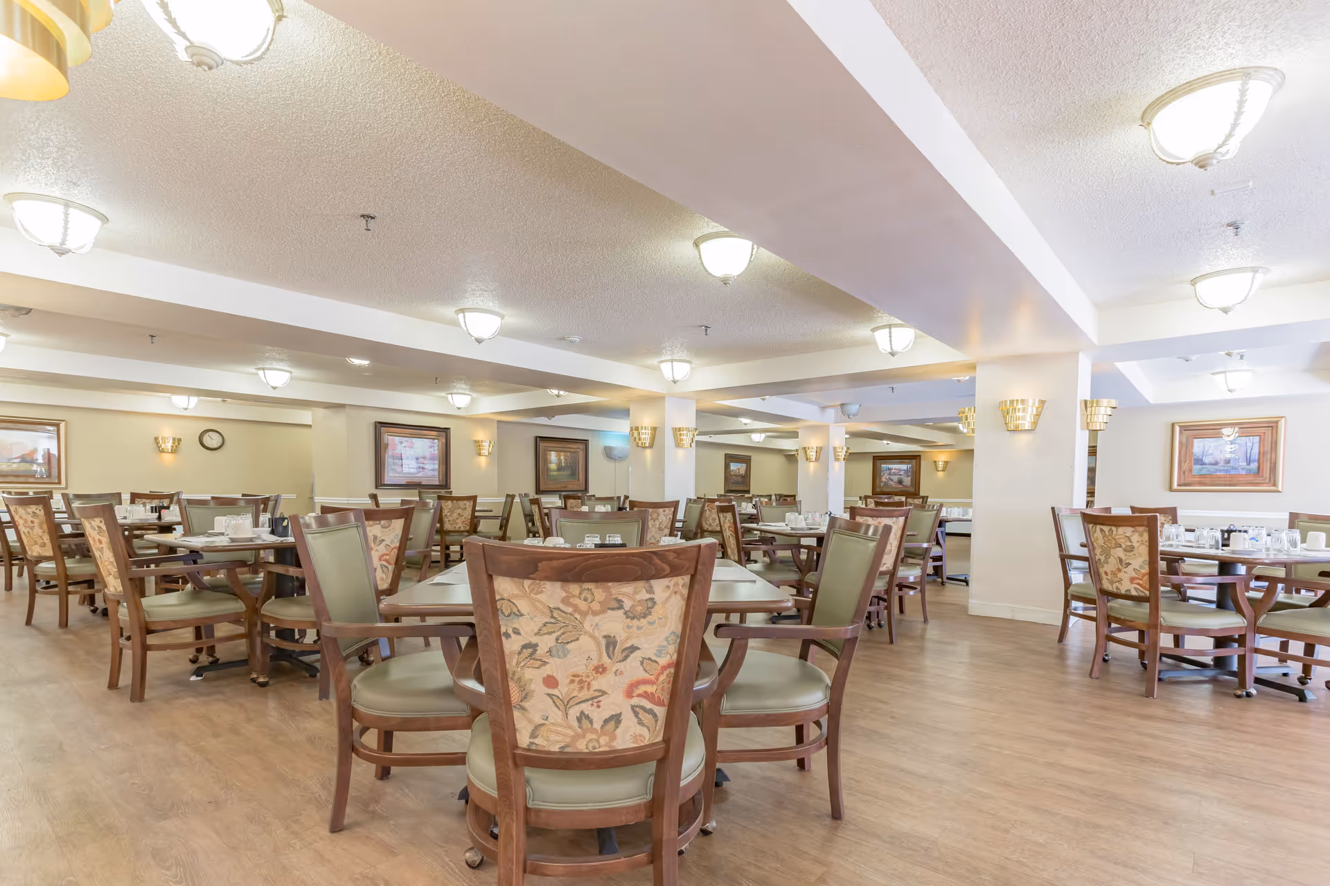 Large dining room with wood floors, round tables set with place settings, and floral-patterned chairs.