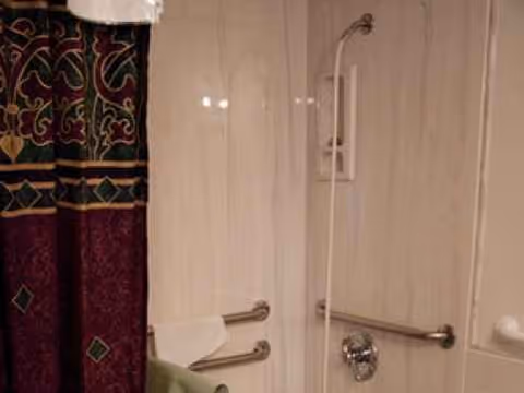 Shower area with grab bars, curtain, and tiled walls in a bathroom.