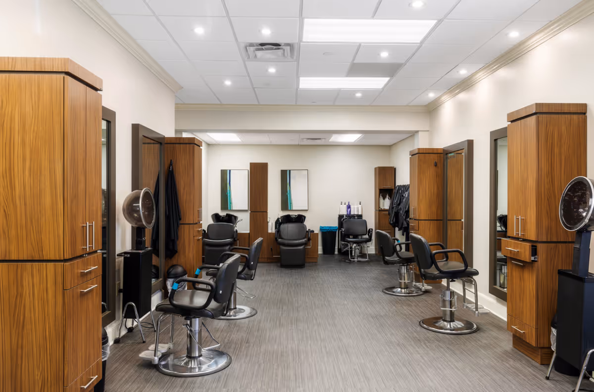 Clean, modern hair salon with styling chairs, wooden cabinetry, mirrors and hairdryers in a well-lit interior.