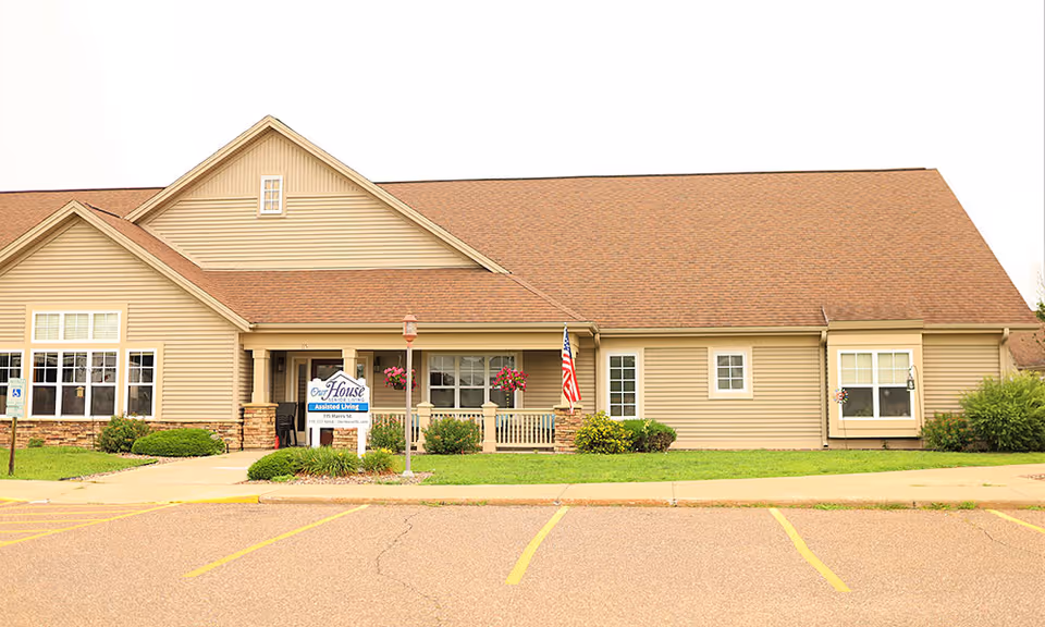 Front exterior of a single-story beige senior living facility with a covered entrance, American flag, and landscaped lawn.