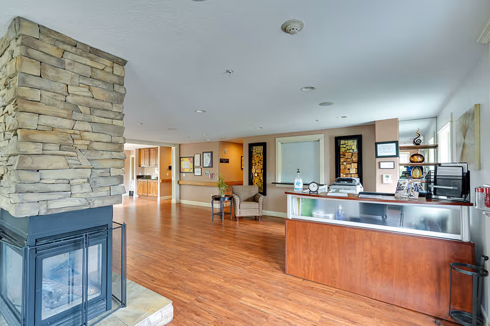 Spacious senior living facility lobby with a stone fireplace, hardwood floors, reception desk, and seating area.