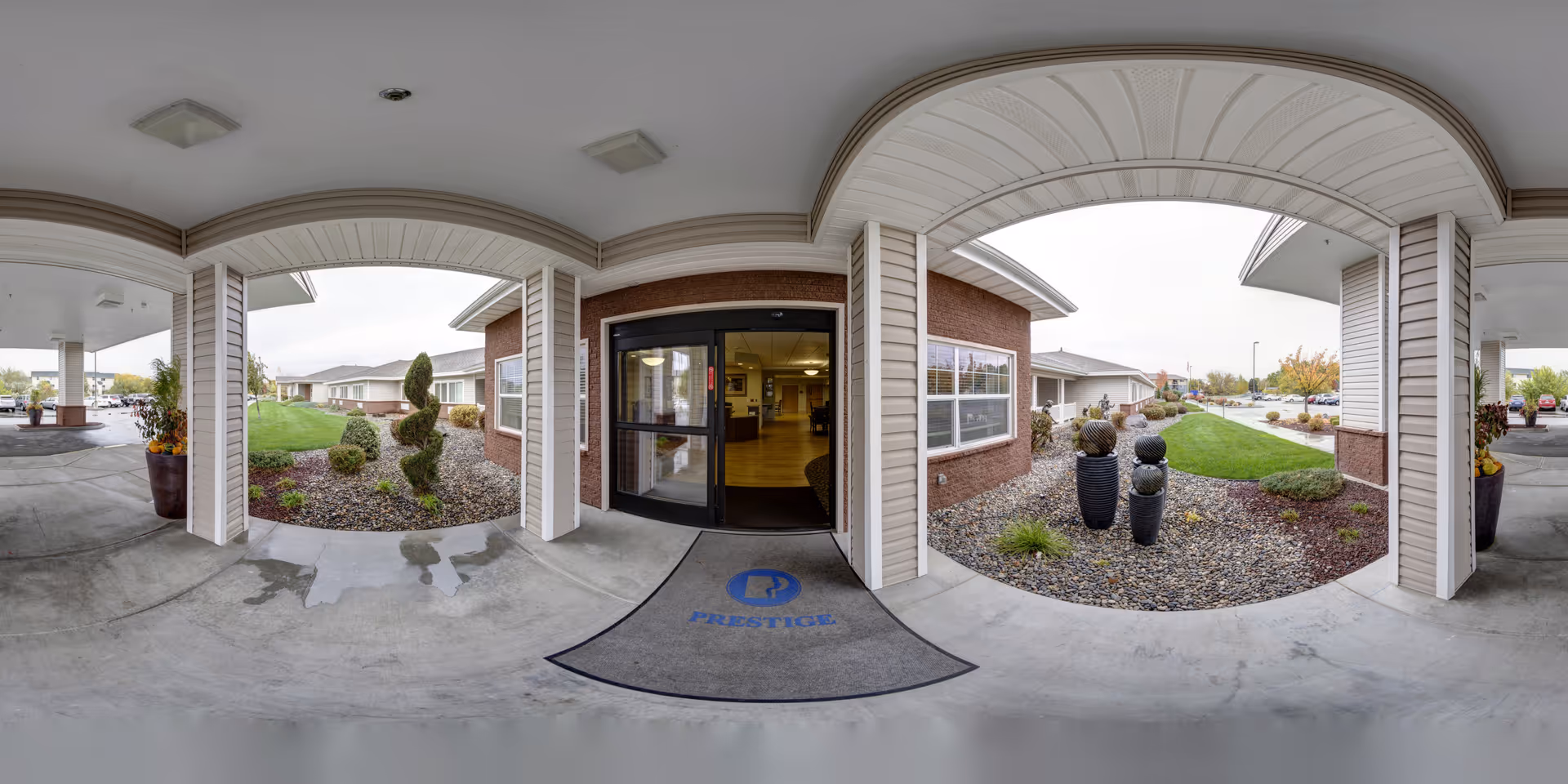 Covered entryway with a glass front door, welcome mat, landscaped beds and decorative planters under a curved canopy.