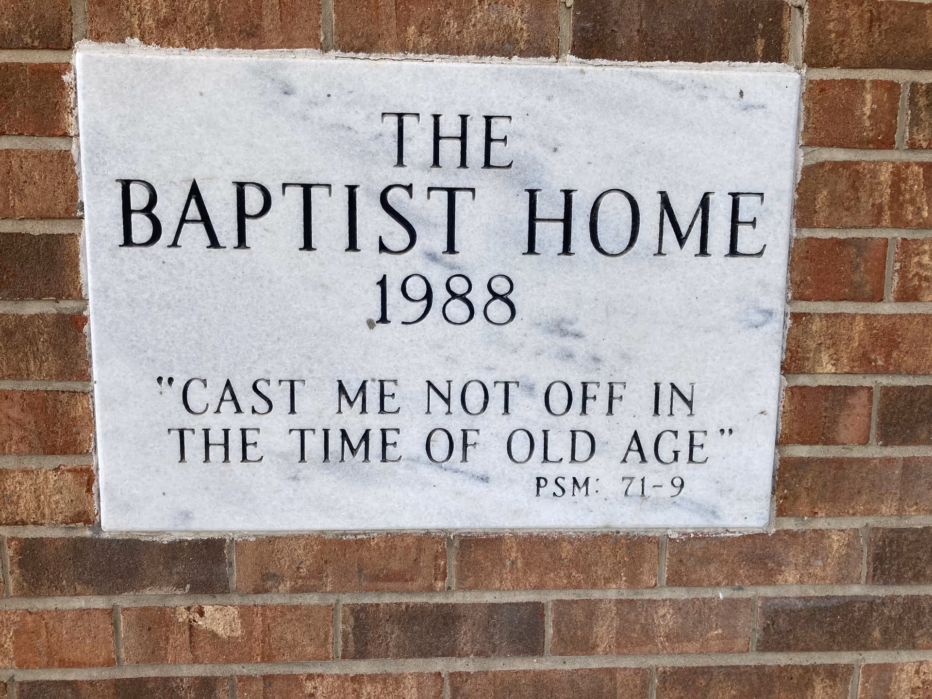 A marble plaque on a brick wall engraved with "THE BAPTIST HOME 1988" and the quote "CAST ME NOT OFF IN THE TIME OF OLD AGE".