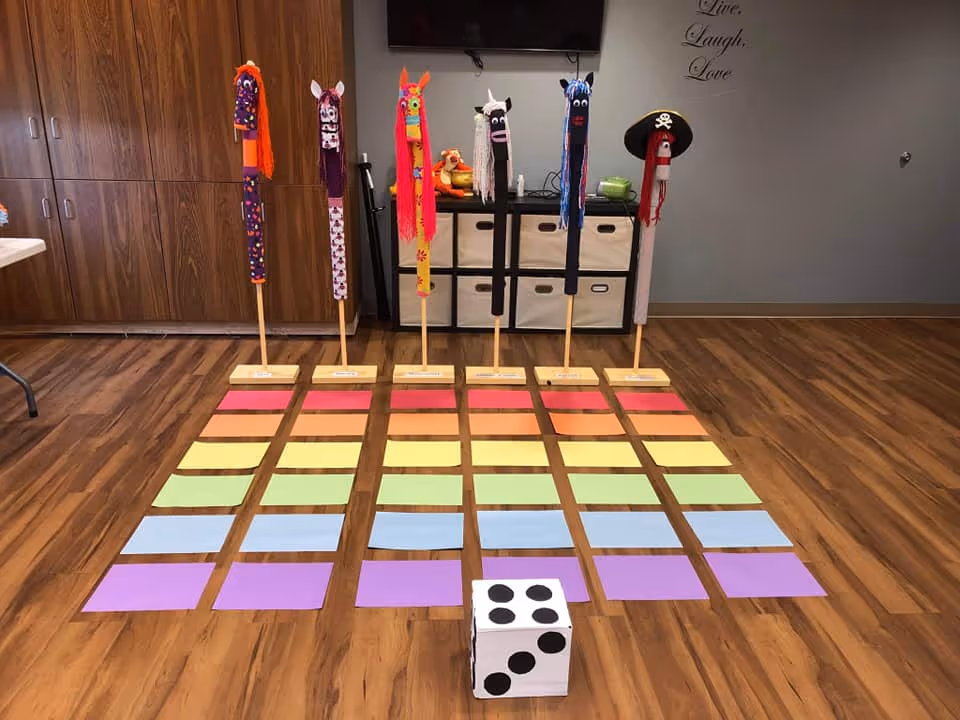 Colorful craft station in a senior facility, with puppet sticks and rainbow mats on wood floor.