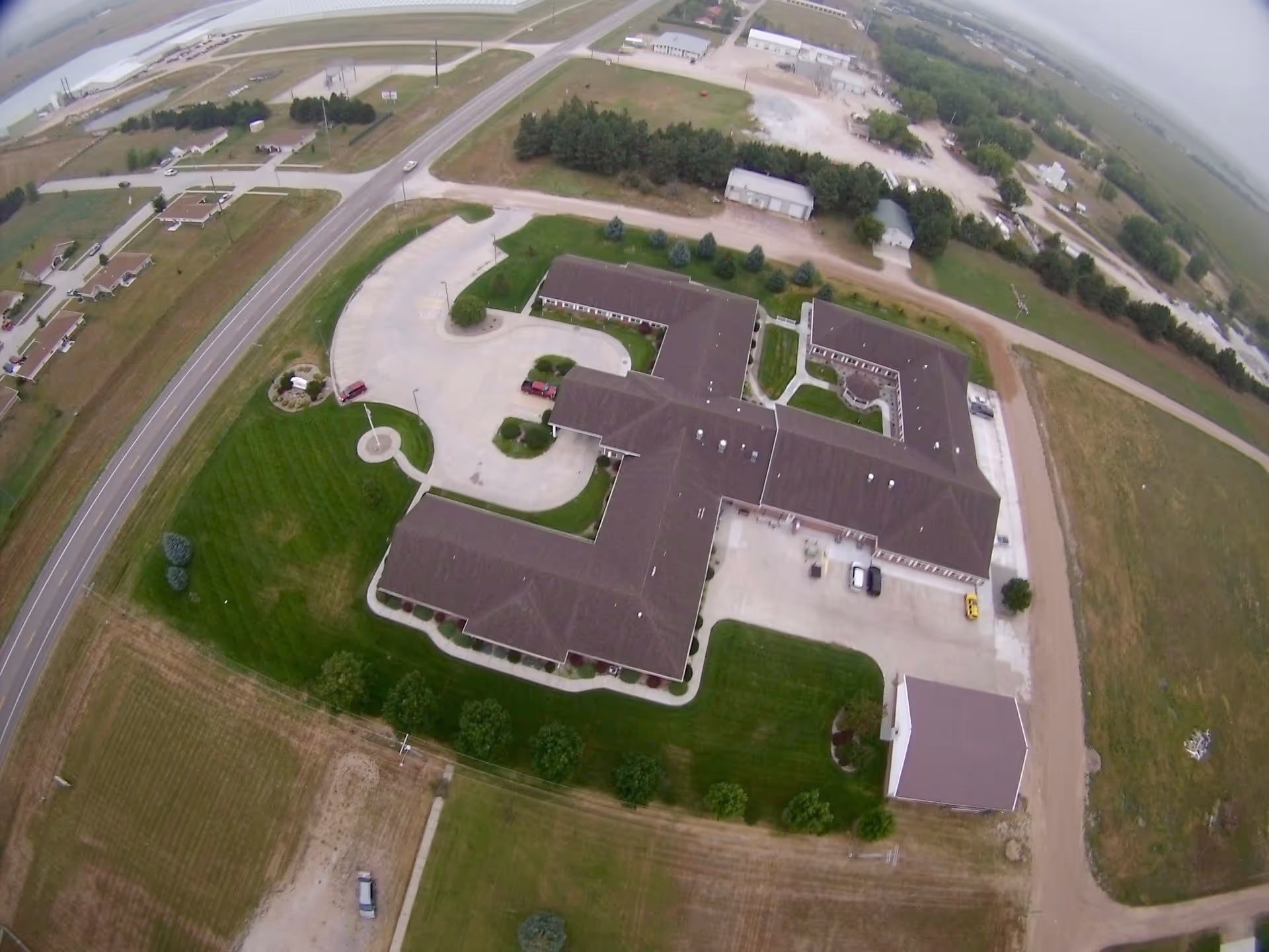 Aerial view of an assisted living campus showing connected single-story buildings, driveways, parking areas and surrounding lawns and roads.