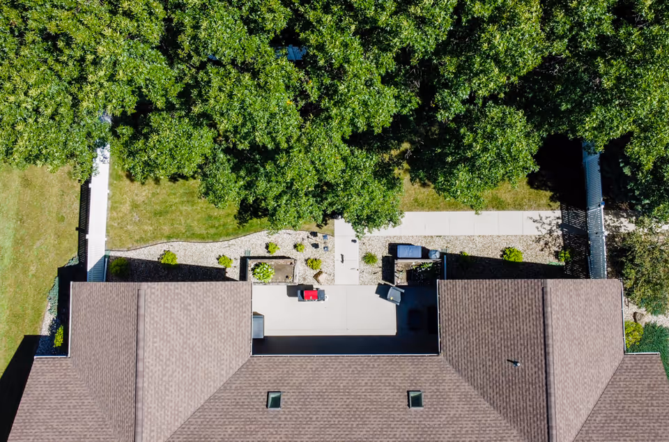 Aerial view of a senior living facility showing the roof of a building with a patio area, surrounded by trees and a walkway.