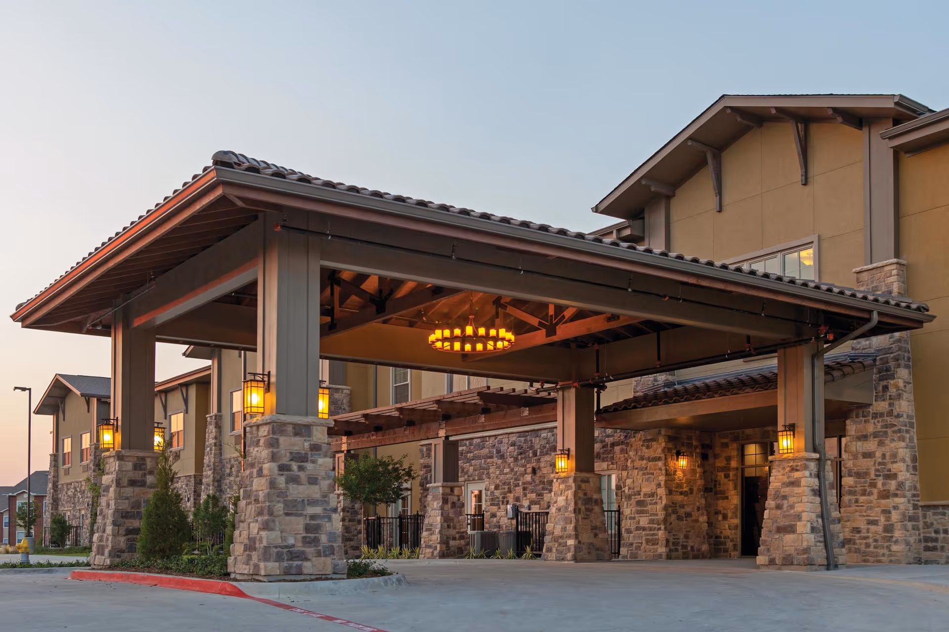 Covered stone-and-timber porte-cochère entrance with hanging lanterns and a chandelier at the front of a multi-story building.