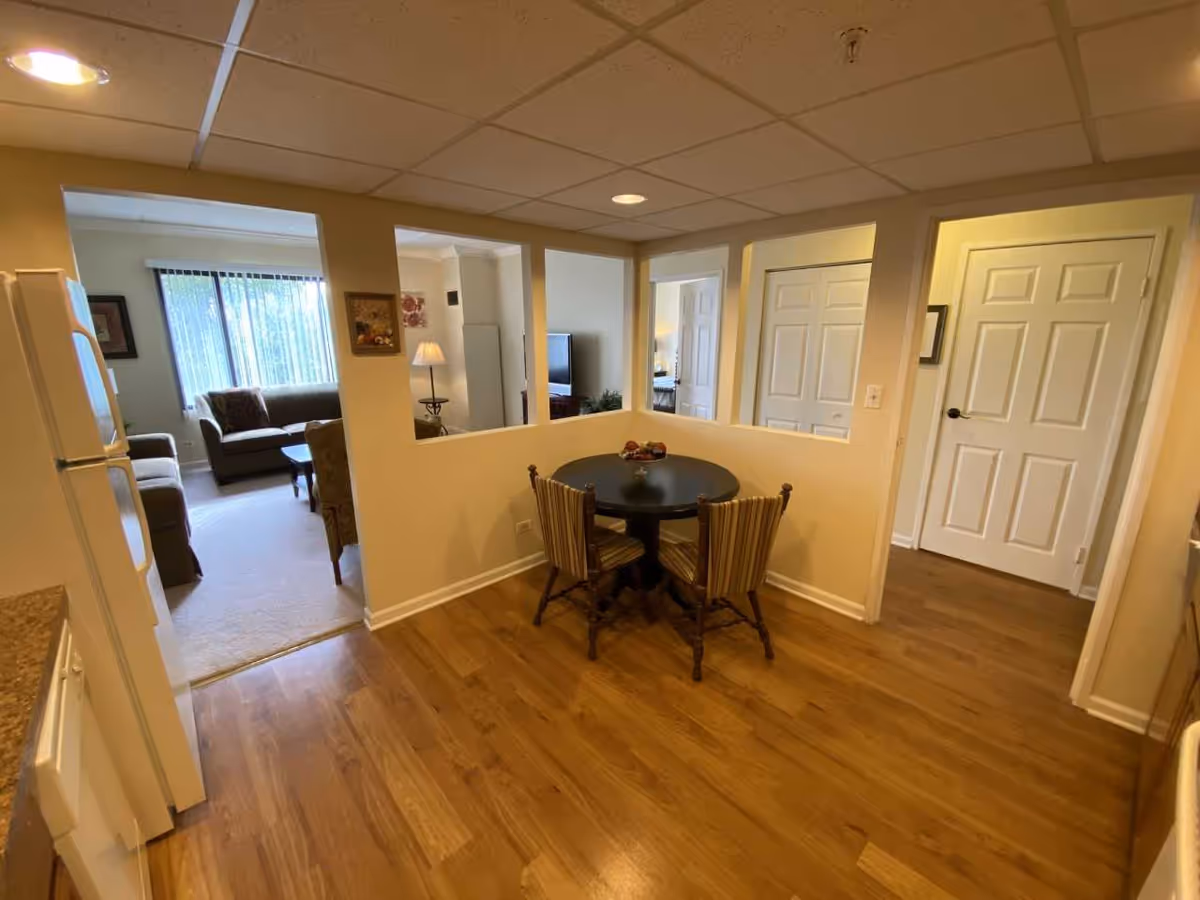 Small dining nook with a round table and chairs opening to a living room and hallway in an apartment.
