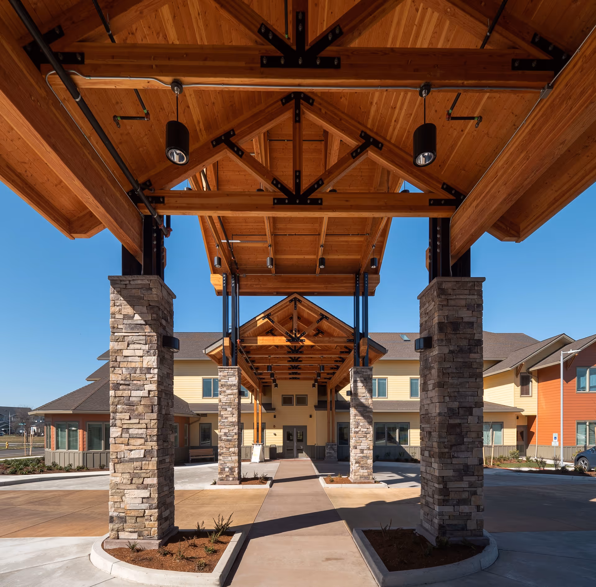 Wooden porte-cochère with stone columns shelters a building entrance at Pear Valley Senior Living.