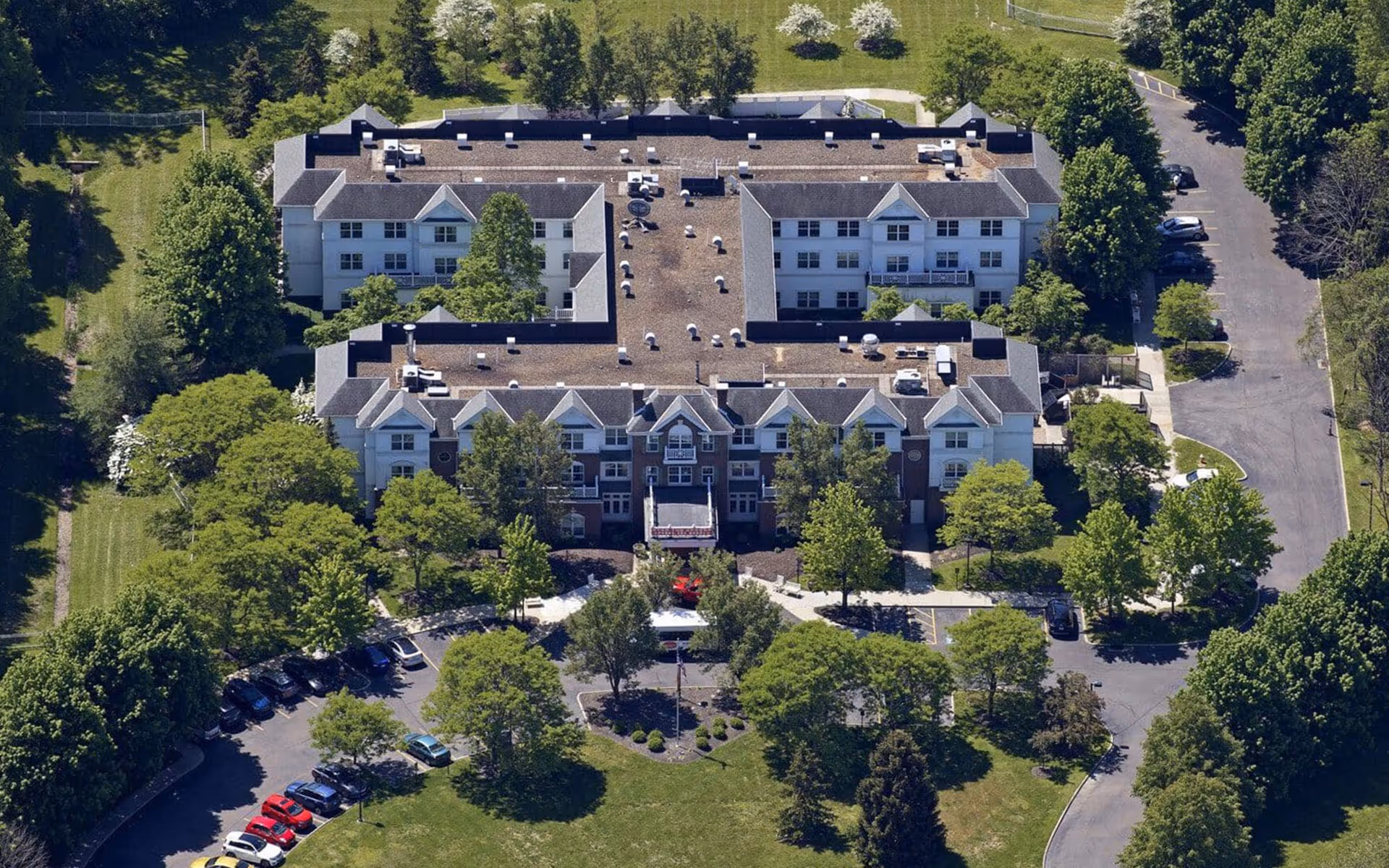 Aerial view of a multi-story senior living building with landscaped grounds, trees, and parking areas.