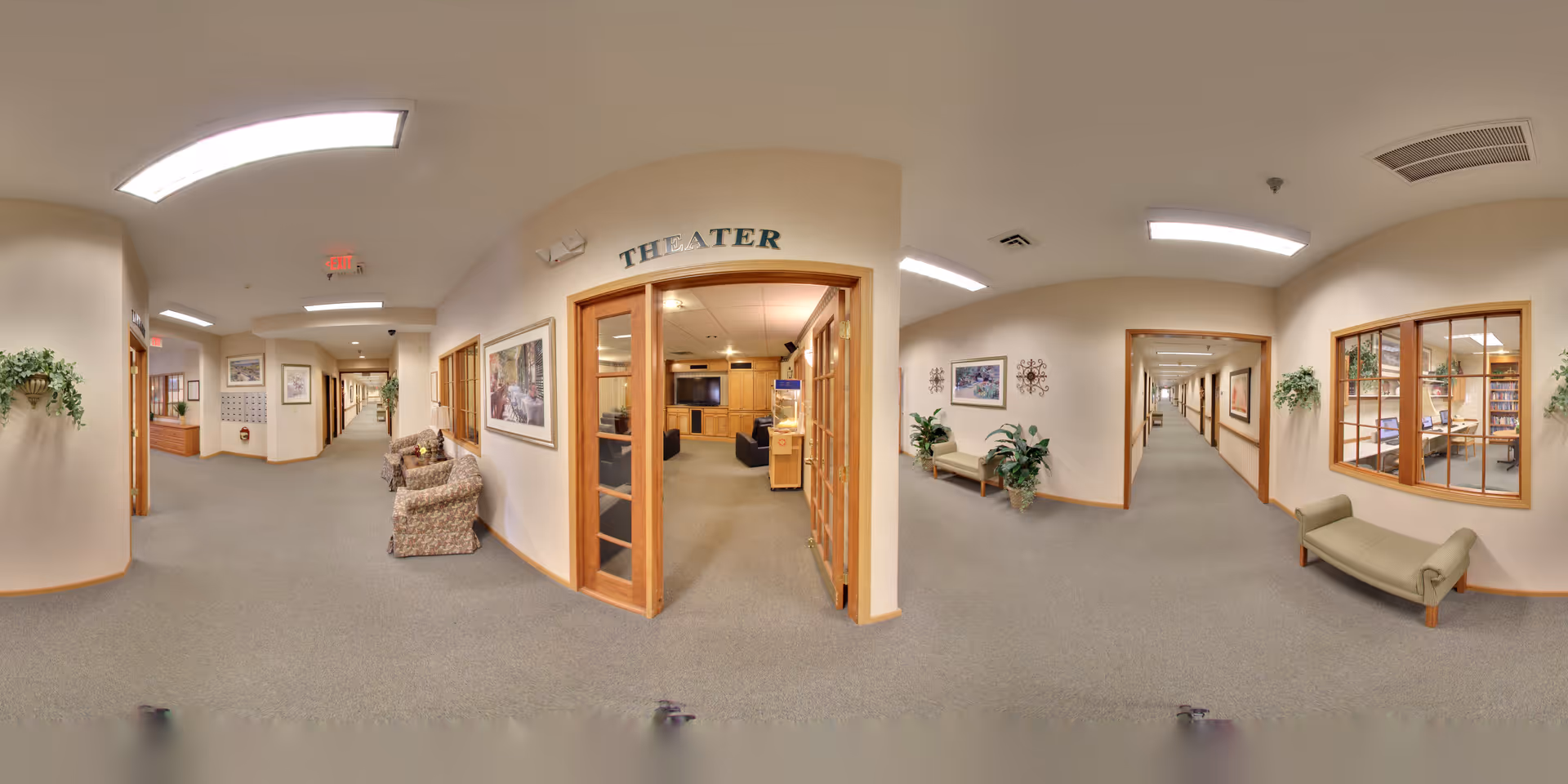 Wide interior hallway of a senior living facility with carpeted floors, seating, plants, and a labeled theater entrance.