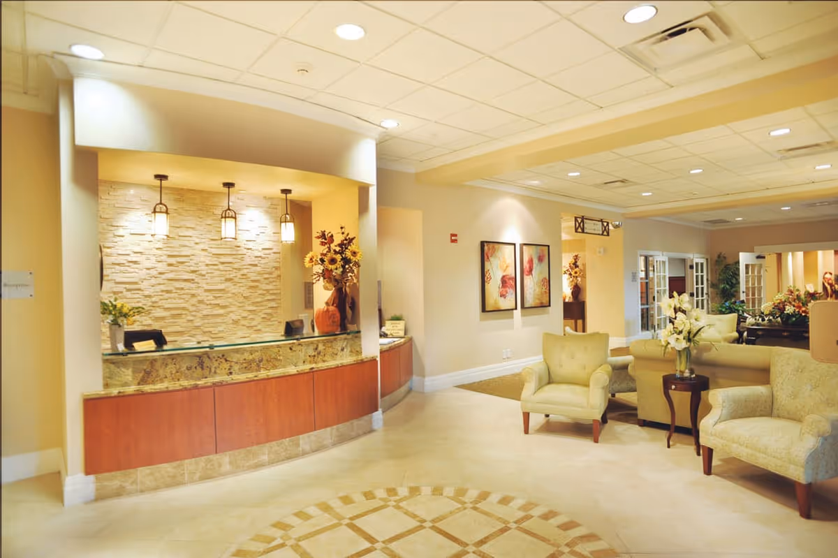 A welcoming lobby reception area featuring a curved desk with a stone backdrop, decorative flowers, and comfortable seating.