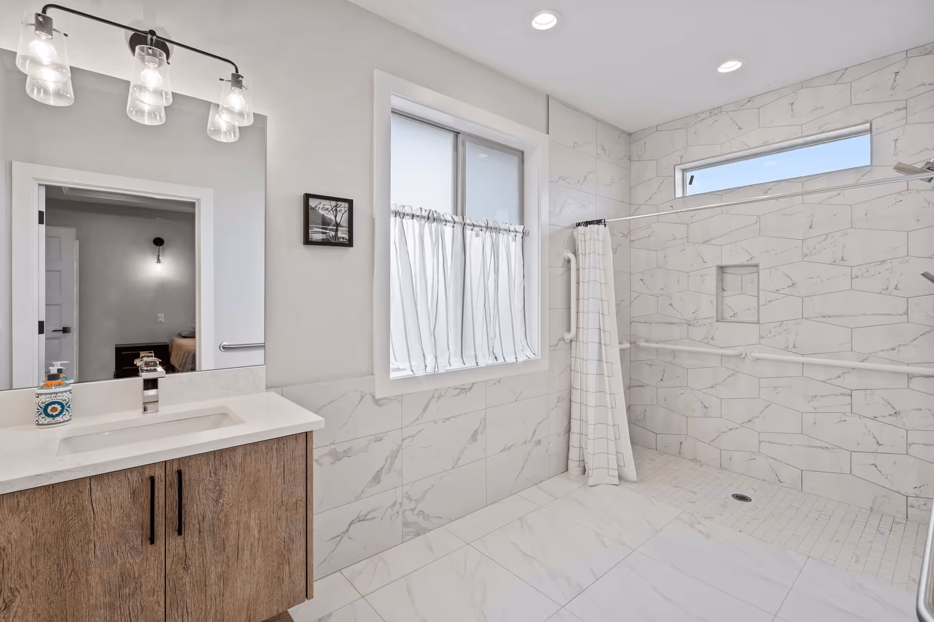 Bright modern bathroom with a walk-in tiled shower with grab bars, a vanity and a window.