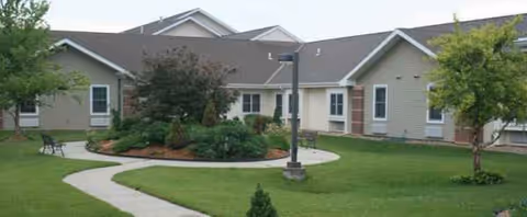 Front view of a senior living building with lawn, curved path, and greenery.