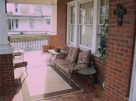 Brick porch with cushioned seating, small table, and potted plant.