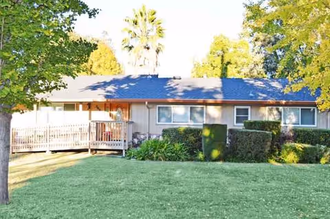 A single-story senior residence with a wooden deck and green lawn in front.