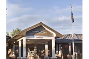 Front exterior view of the Idaho State Veterans Home Boise building with a covered entrance supported by white columns, a sign displaying the facility name, and a flagpole with a flag flying beside the entrance.