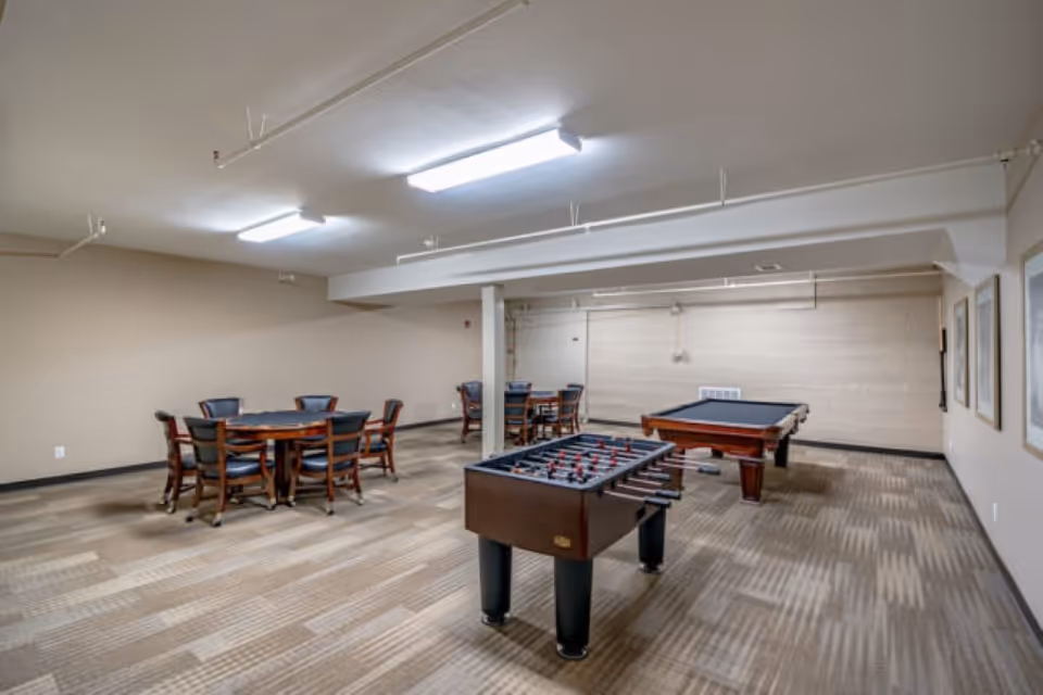 Recreation room with a foosball table, pool table, and several round card tables and chairs.
