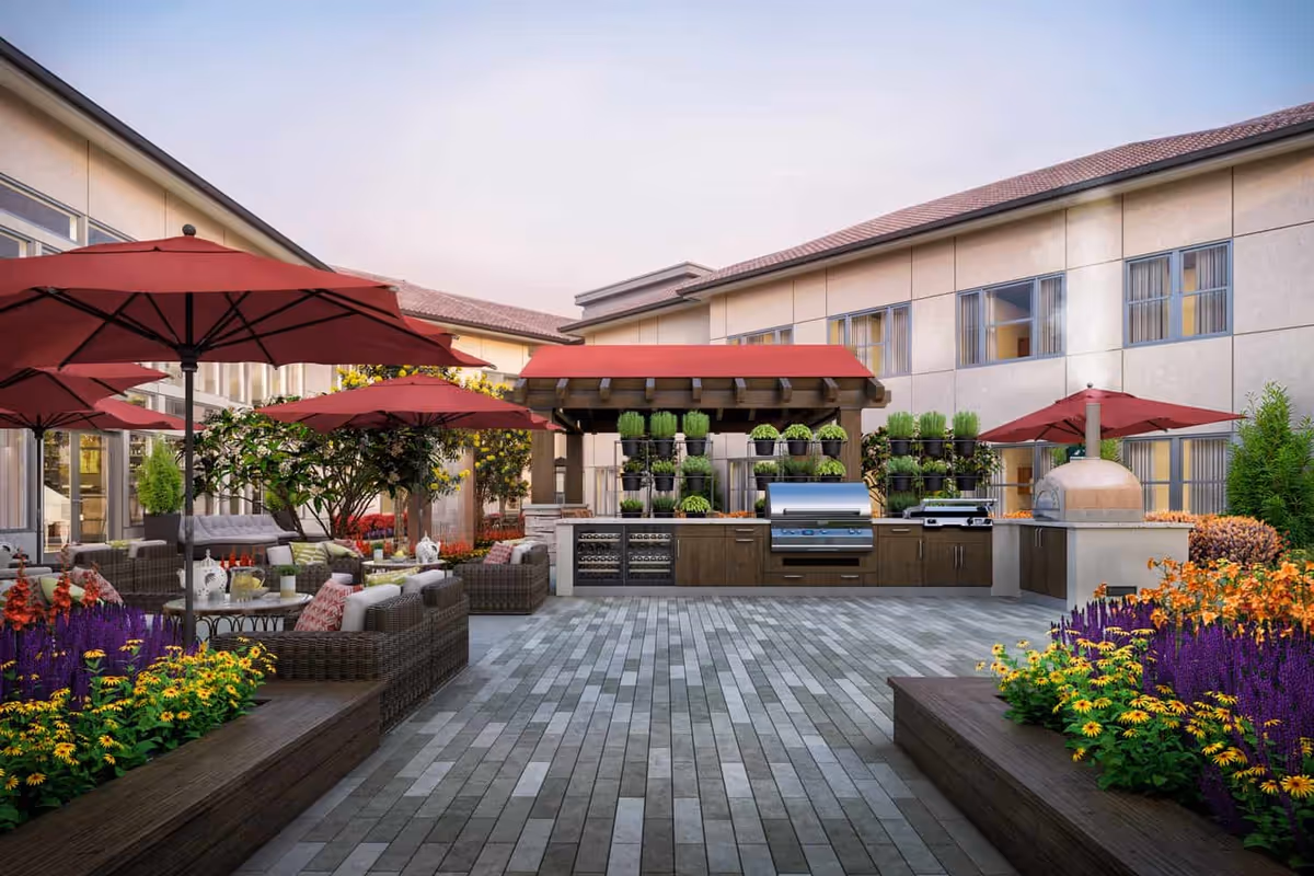 Outdoor courtyard patio with seating, red umbrellas, a grilling station and flower beds.