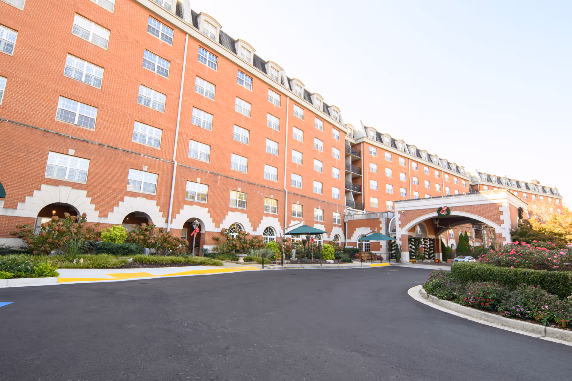 Large red-brick multi-story retirement community building with a covered driveway entrance and landscaped gardens.