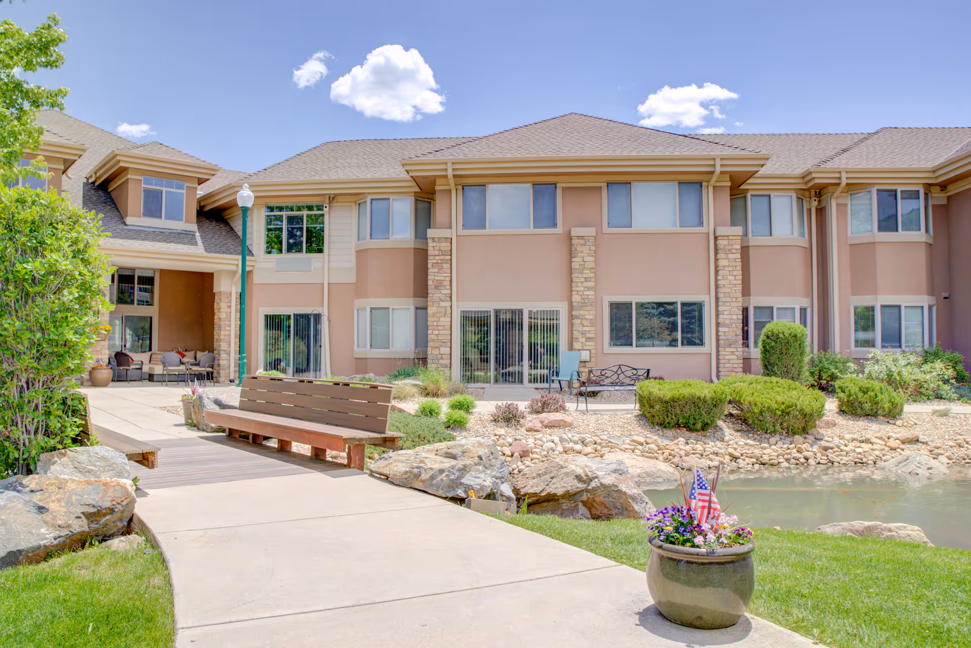 Front exterior of Golden Pond Senior Living showing a landscaped courtyard with a bench, pond, and the two-story building.