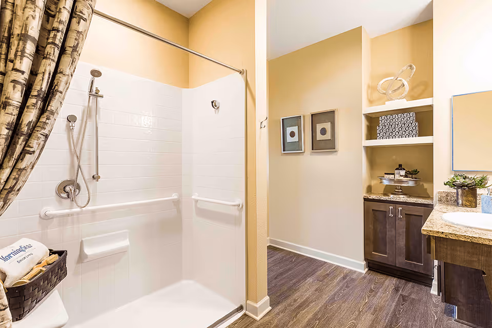 Bright accessible bathroom with a tiled walk-in shower with grab bars, shower curtain, and a vanity with shelving.